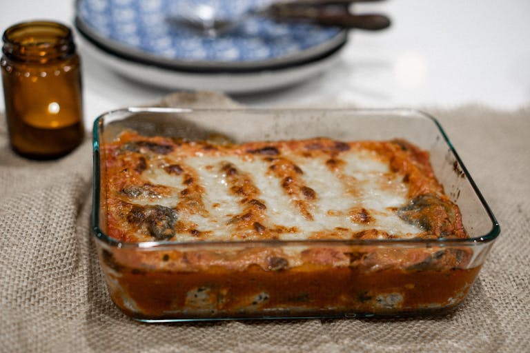 Savory baked lasagna in a glass tray on a burlap tablecloth, ready to serve.