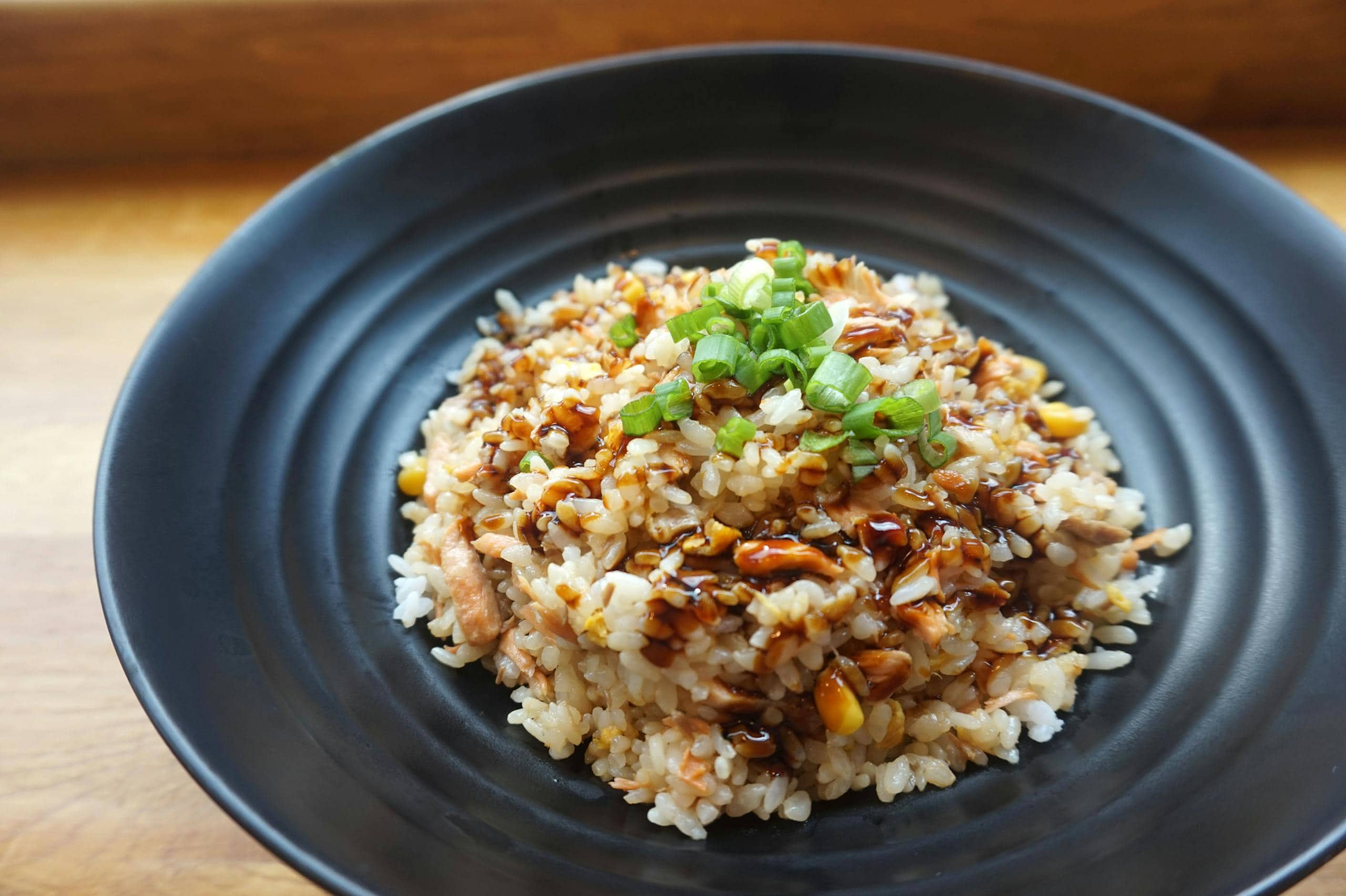 Delicious homemade fried rice with scallions and sauce on a black plate.